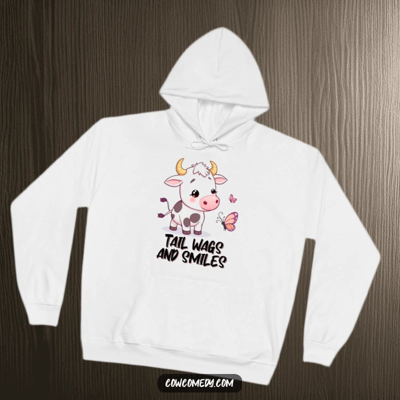 Funny Hoodie depicting a cow joyfully wiggling its tail near a cartoon butterfly, offering warmth and whimsical farm fun.
